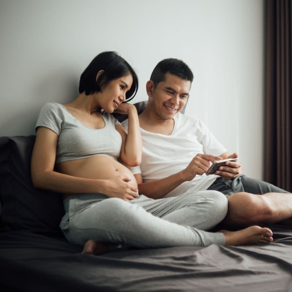 Beautiful pregnant woman and her husband are holding ultrasound scan smartphone on the bed at home.