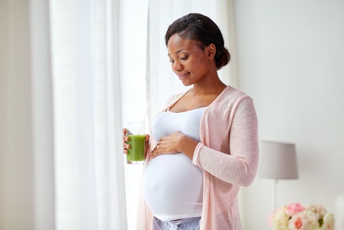 happy pregnant african american woman drinking green smoothie at home